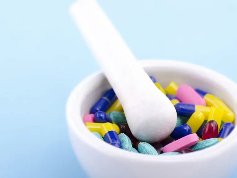 Mortar and pestle filled with colorful capsules and tablets, representing custom compounding